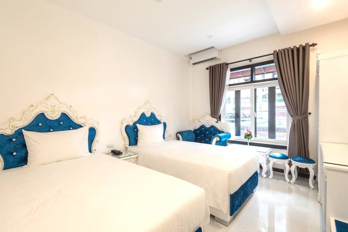 A hotel room with two beds, a small table, and a window with curtains.