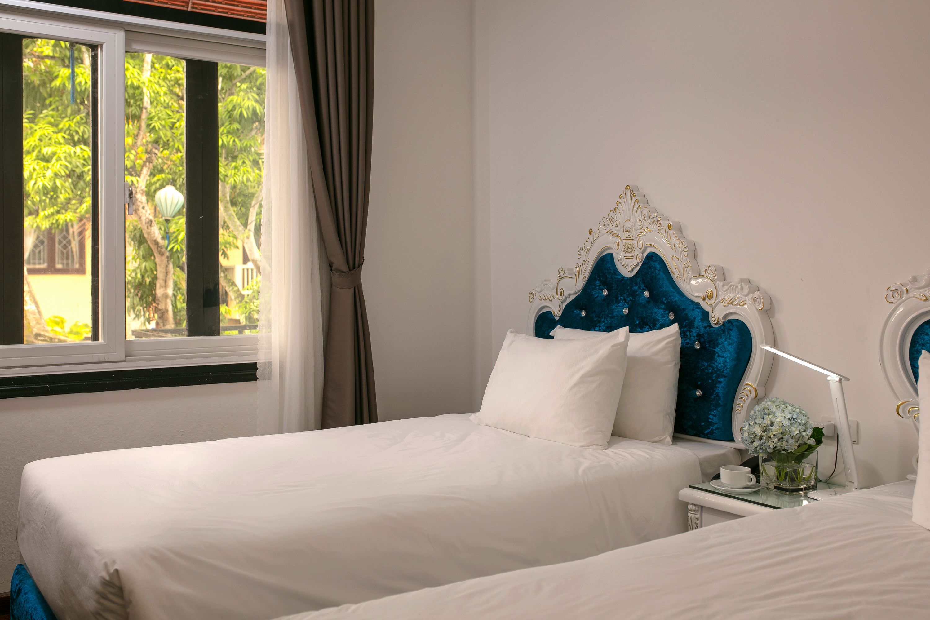 A bedroom with two beds, a nightstand, a lamp, and a window with curtains.