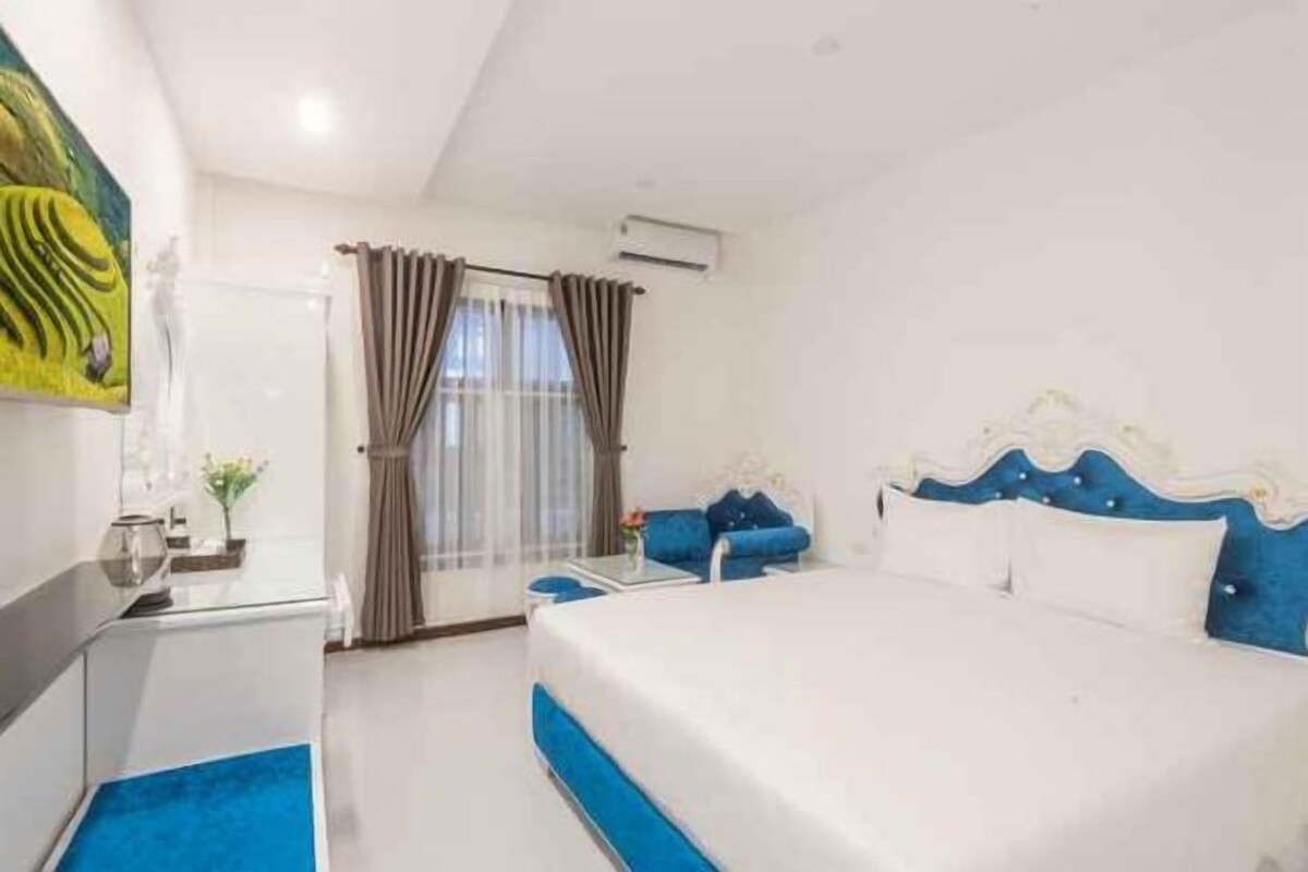 A hotel room with a bed, a desk, a chair, and a window with curtains.