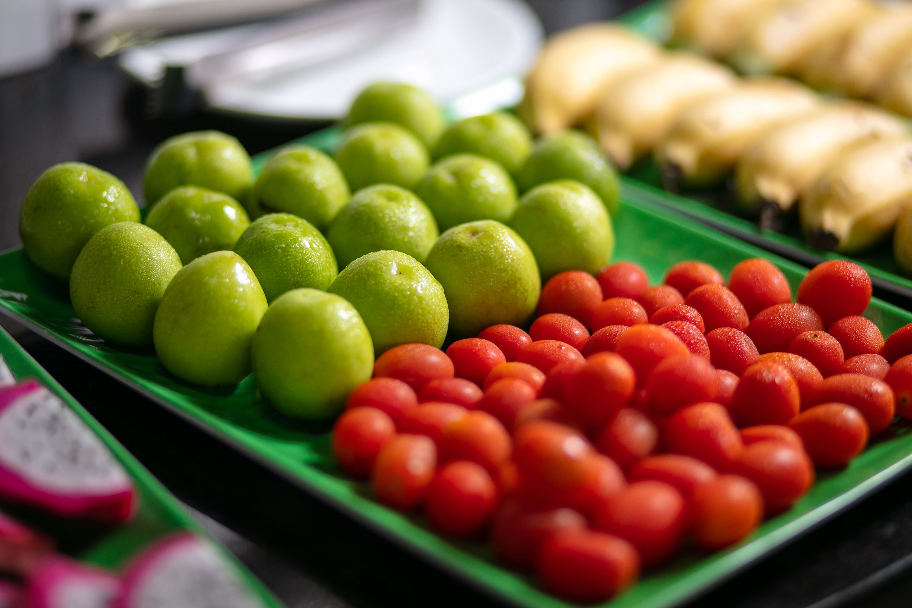 Variedad de frutas como manzanas verdes, tomates rojos y plátanos amarillos sobre una bandeja verde.