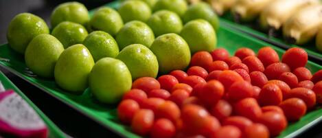 Variedad de frutas como manzanas verdes, tomates rojos y plátanos amarillos sobre una bandeja verde.