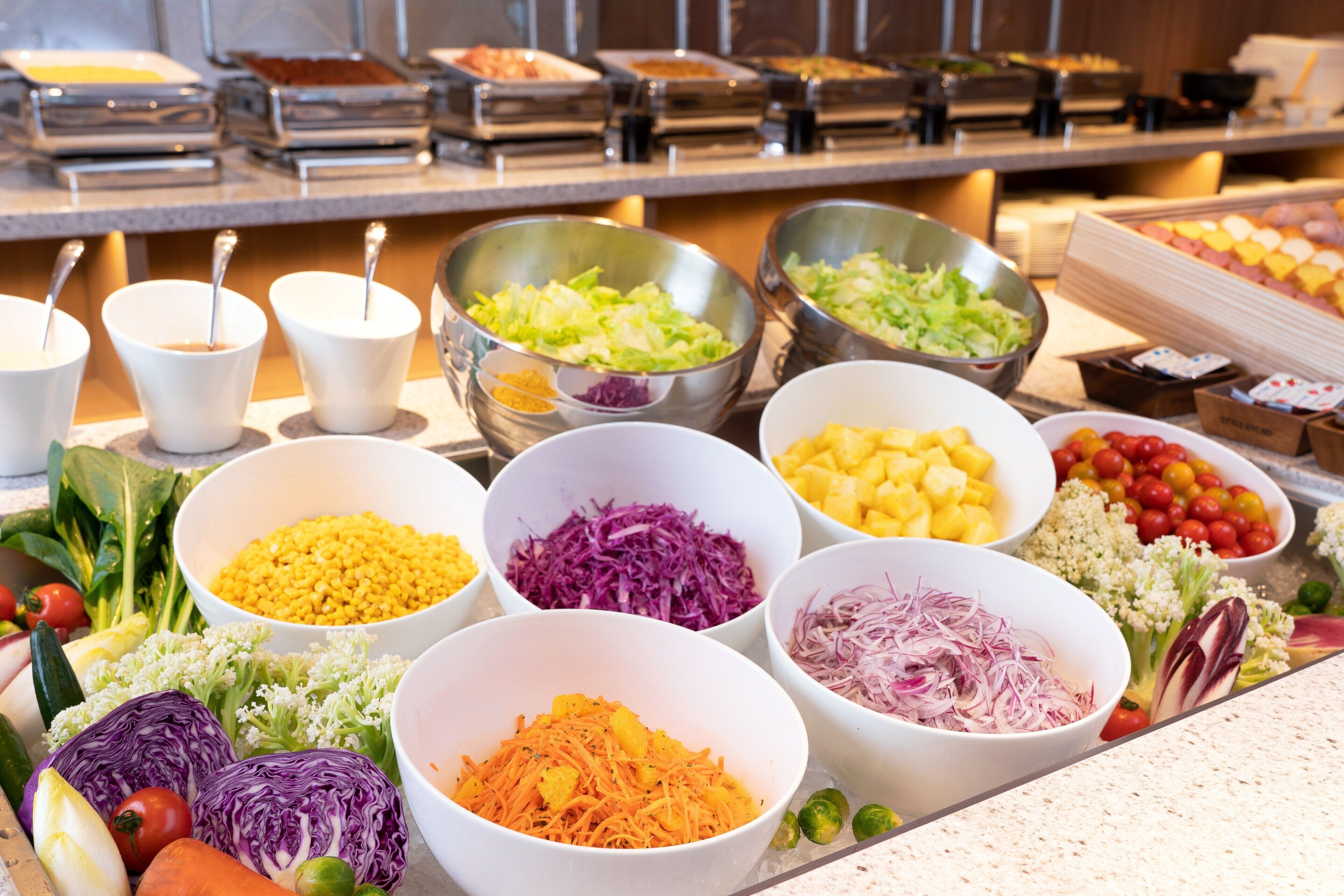 A buffet with various food items in bowls, including vegetables and fruits.