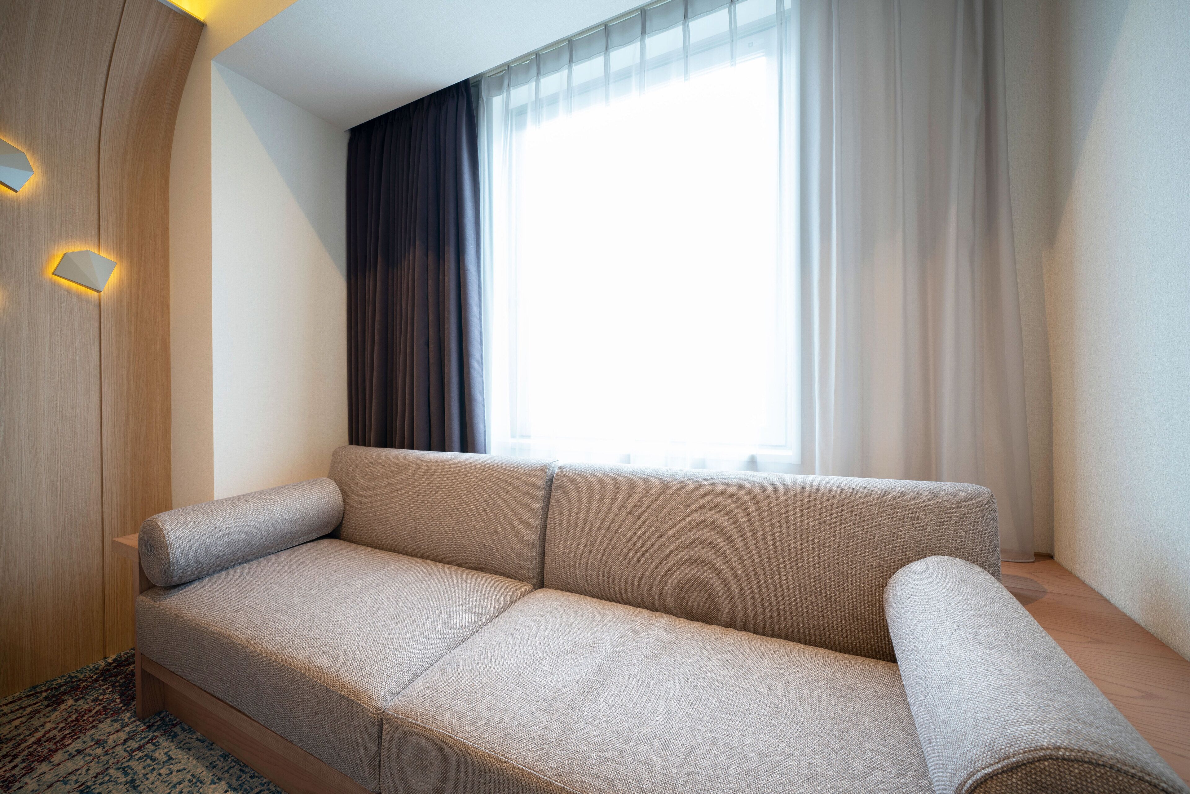 A modern living room with a sofa, a wooden accent wall, and a large window with curtains.