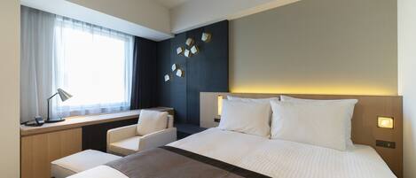 Une chambre d’hôtel avec un grand lit, un bureau avec une chaise, une fenêtre avec des rideaux et un mur décoré d’œuvres d’art géométriques.