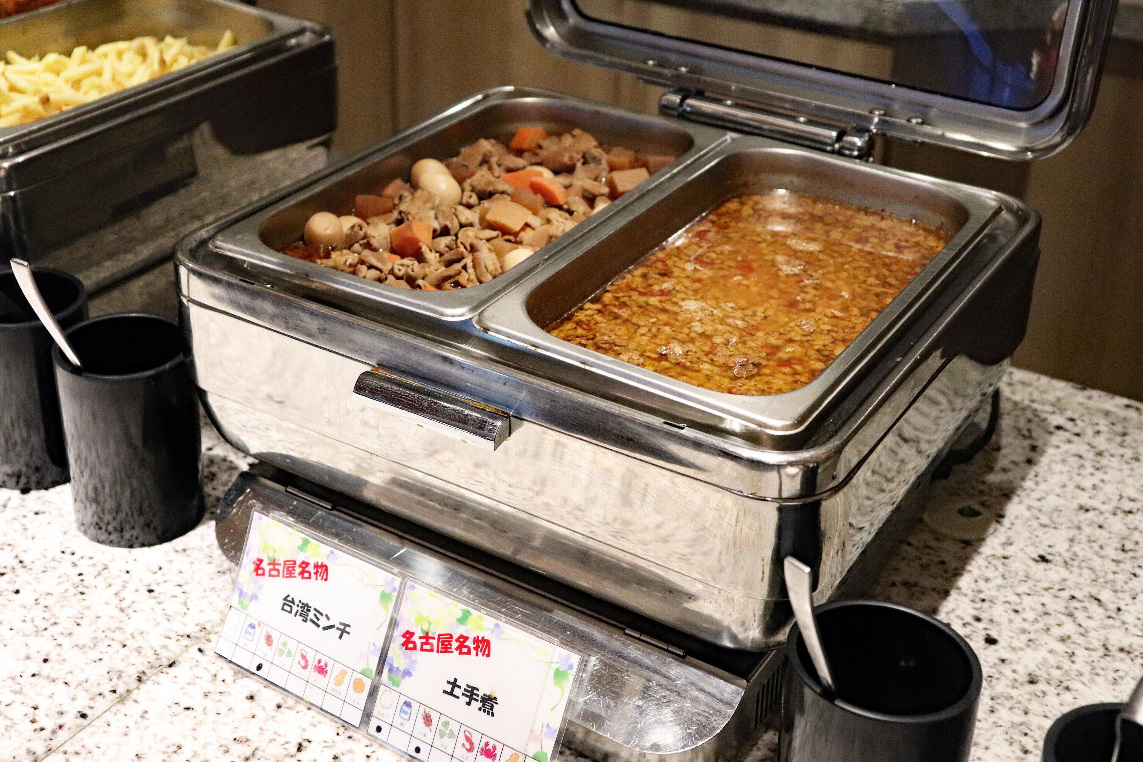 A buffet with various dishes including meats, vegetables, and a large container of chili.