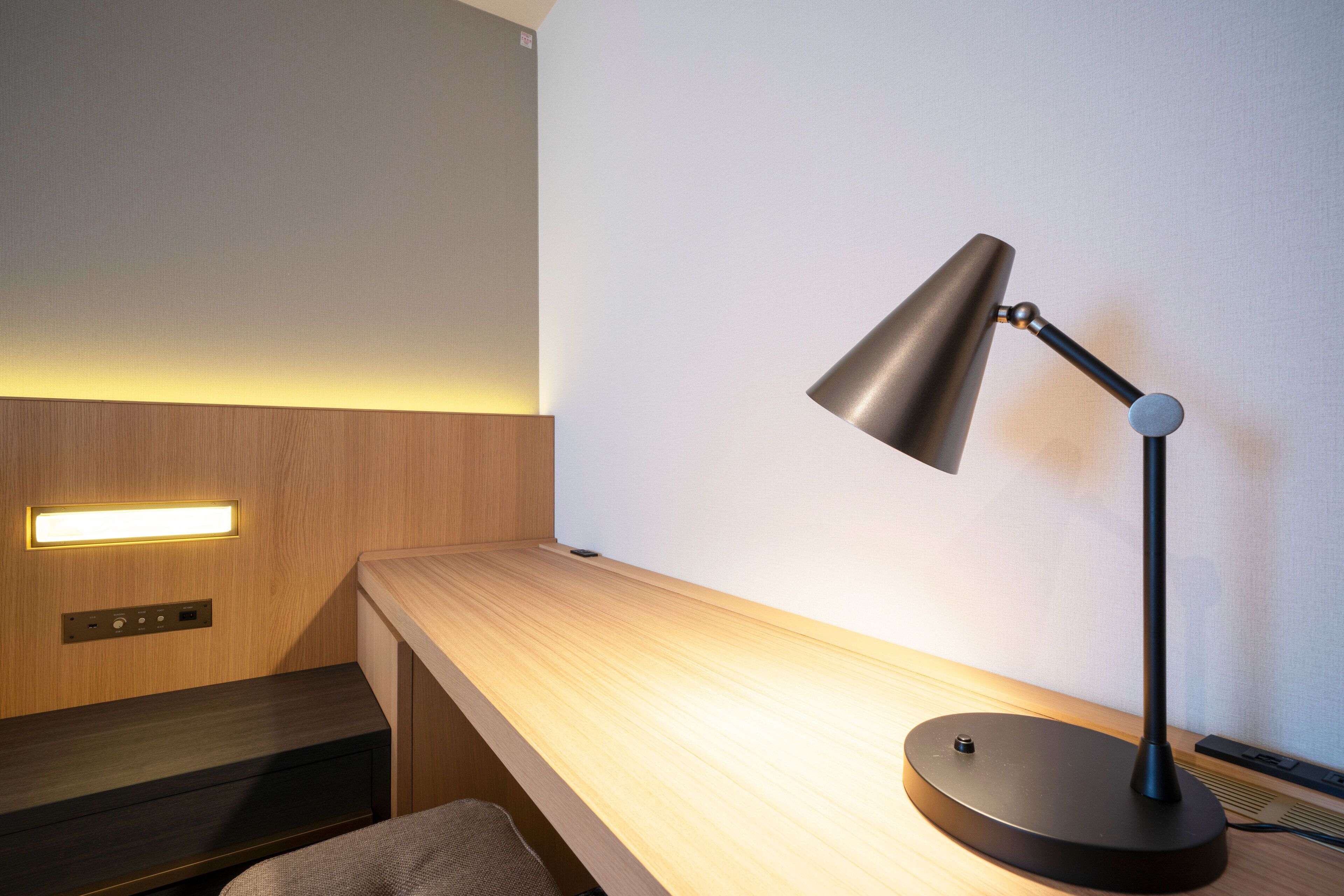 Ein modernes Zimmer mit einem Holztisch, einer schwarzen Schreibtischlampe und Wandleuchte.