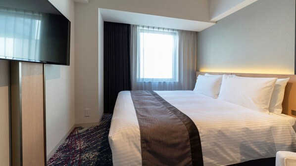 A hotel room with a bed, a flat-screen TV, a window with curtains, and a carpeted floor.