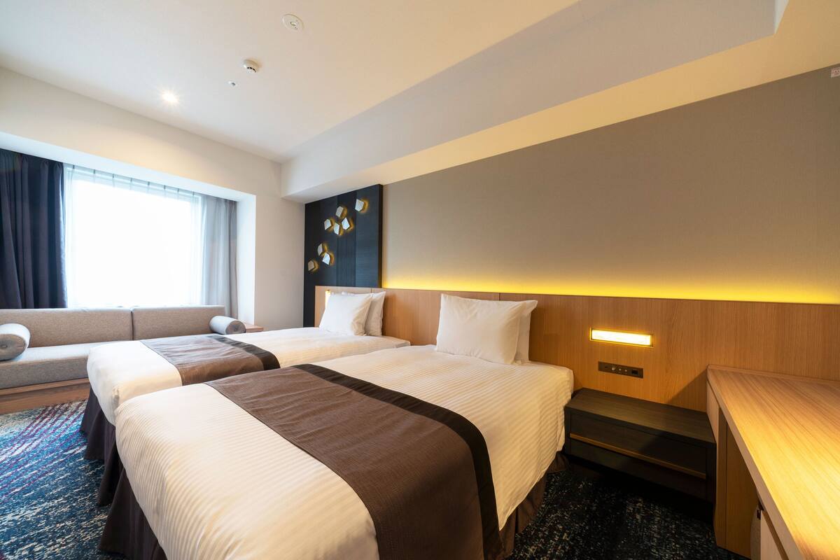 Une chambre d’hôtel avec deux lits, un canapé, un bureau et un luminaire fixé au mur.