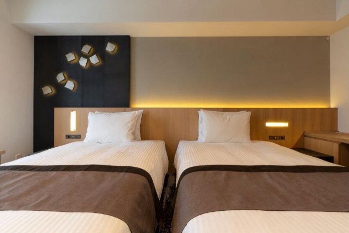 A hotel room with two beds, a dark accent wall, and a modern light fixture.
