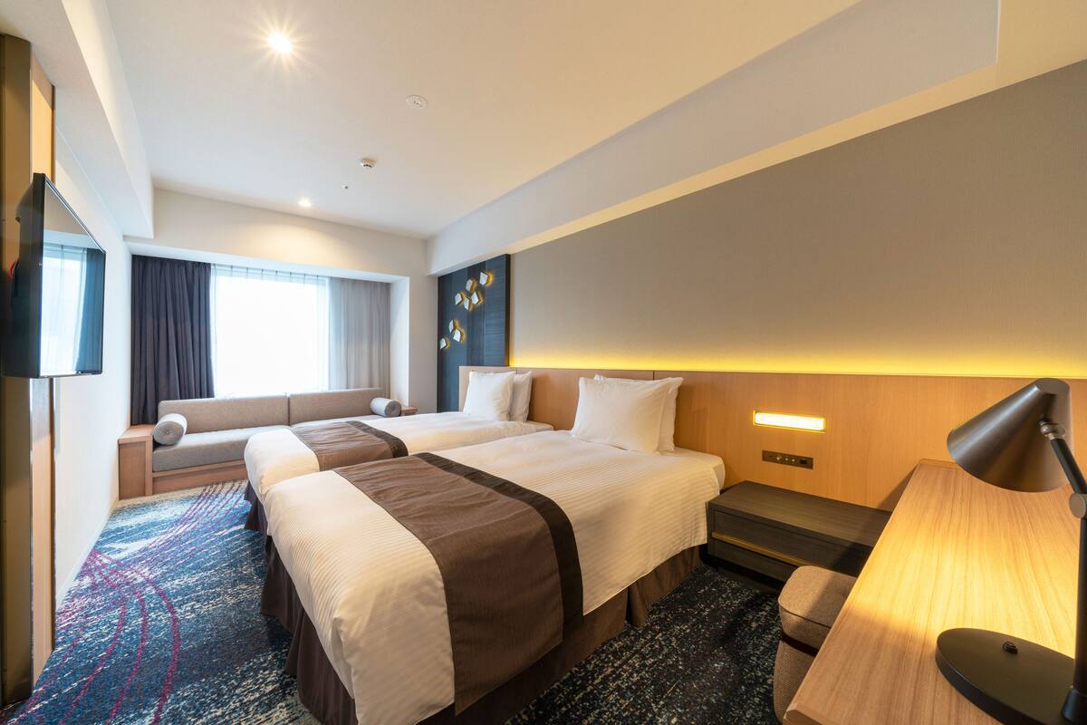 Une chambre d’hôtel avec deux lits, un canapé, un bureau et une lampe.