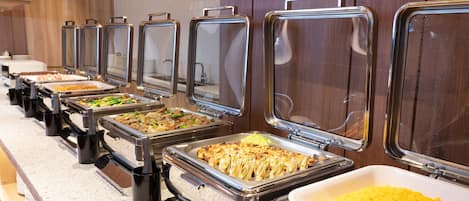 Un bufé con diversos alimentos presentados en bandejas metálicas.