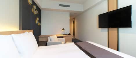 A hotel room with a large bed, a desk with a chair, a flat-screen TV, and a wall-mounted TV.
