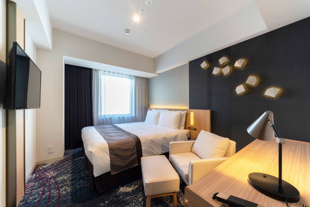 Une chambre d’hôtel avec deux lits, un bureau, une chaise, une télévision et une fenêtre avec des rideaux.