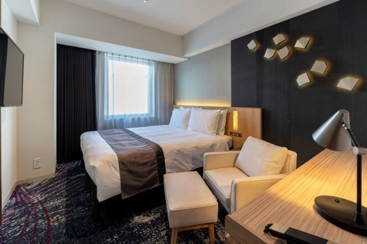 A hotel room with two beds, a desk, a chair, a desk lamp, and a TV.