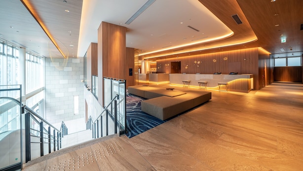 A modern hotel lobby with a spacious seating area, a reception desk, and a staircase leading to an upper level. - Hotel JAL City Nagoya Nishiki (Nagoya)