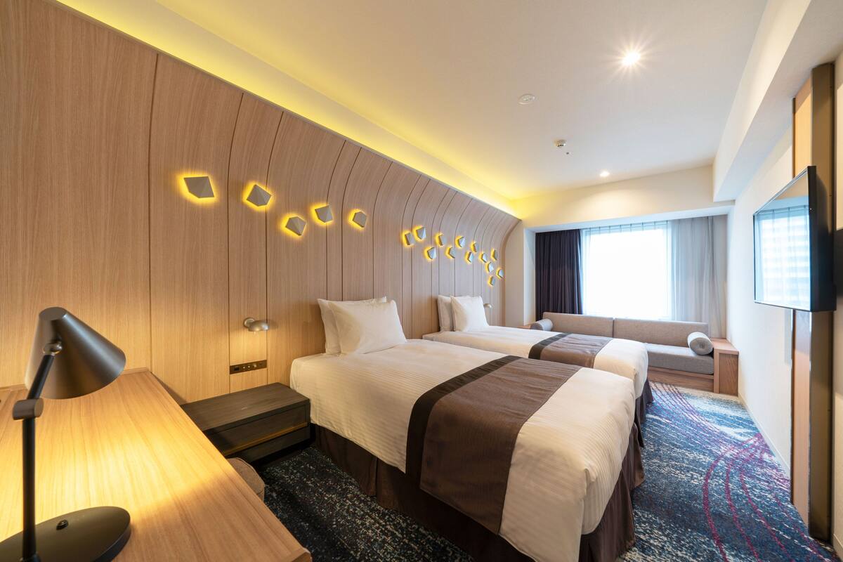 Une chambre d ’hôtel avec deux lits, un bureau, une lampe, une télévision et une fenêtre avec des rideaux.