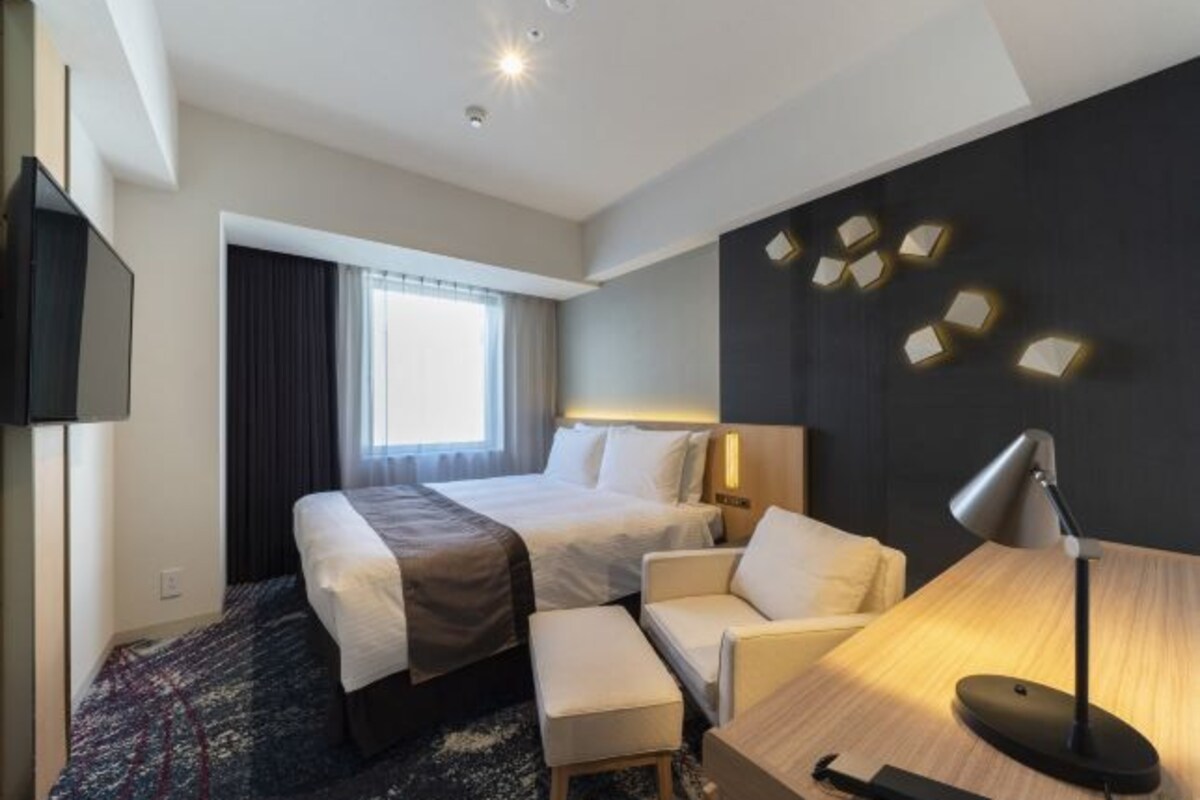 A hotel room with two beds, a desk, a chair, a TV, and a window with curtains.