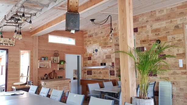 Un intérieur rustique en bois, avec une longue table à manger, des chaises et des luminaires suspendus.