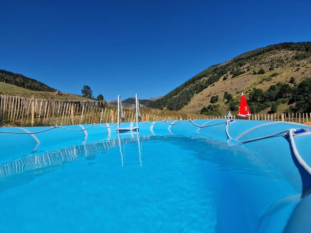 A clear blue pool with a wooden fence and a red flag on a hill.