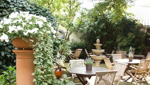 An outdoor patio with wooden chairs and tables, surrounded by lush greenery and a decorative fountain. - Am Glockenturm (Luechow)