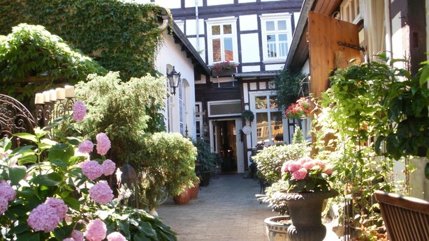 A narrow cobblestone street flanked by traditional half-timbered buildings with potted plants and flowers. - Am Glockenturm (Luechow)