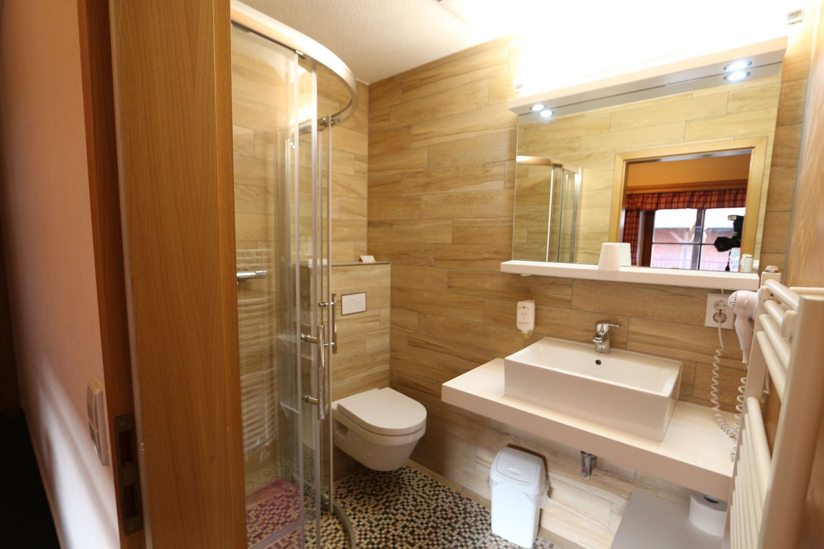 A bathroom with a shower, toilet, sink, and mirror.