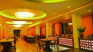 Un restaurante con varias mesas y sillas, un candelabro y una zona de recepción con un muro decorativo.