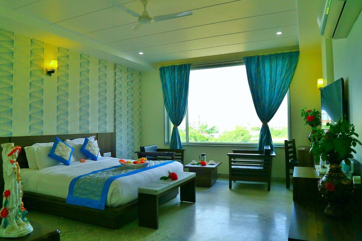 A hotel room with a bed, a desk, a chair, a small table, and a window with curtains.