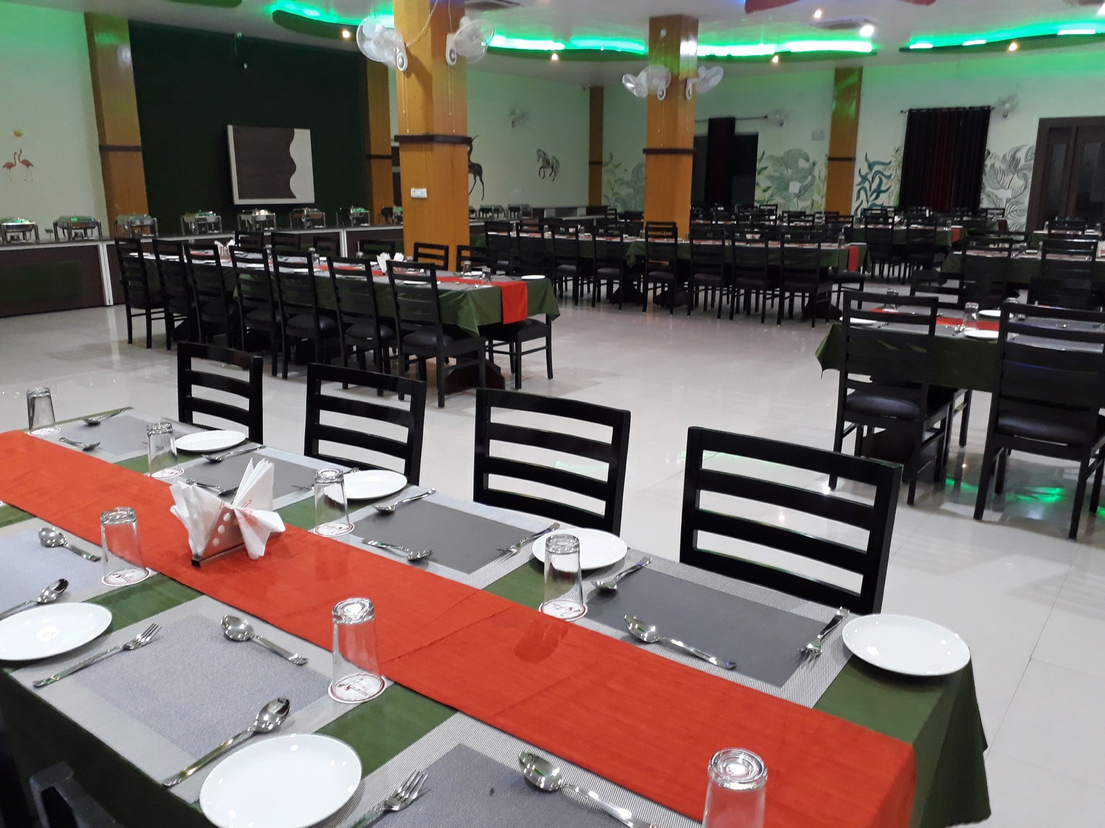 A large banquet hall with multiple tables set for dining, featuring green and red tablecloths and black chairs.