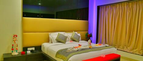 A modern bedroom with a large bed, bedside tables, a bench, and a large window with curtains.