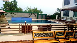 Una piscina con solárium empinado, un banco de madera y un área de descanso con un edificio blanco al fondo.