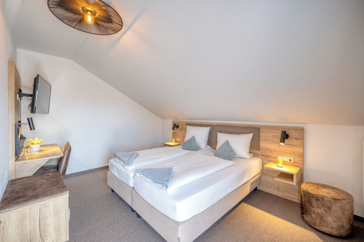 A modern bedroom with a large bed, bedside tables, a desk, and a round ottoman.