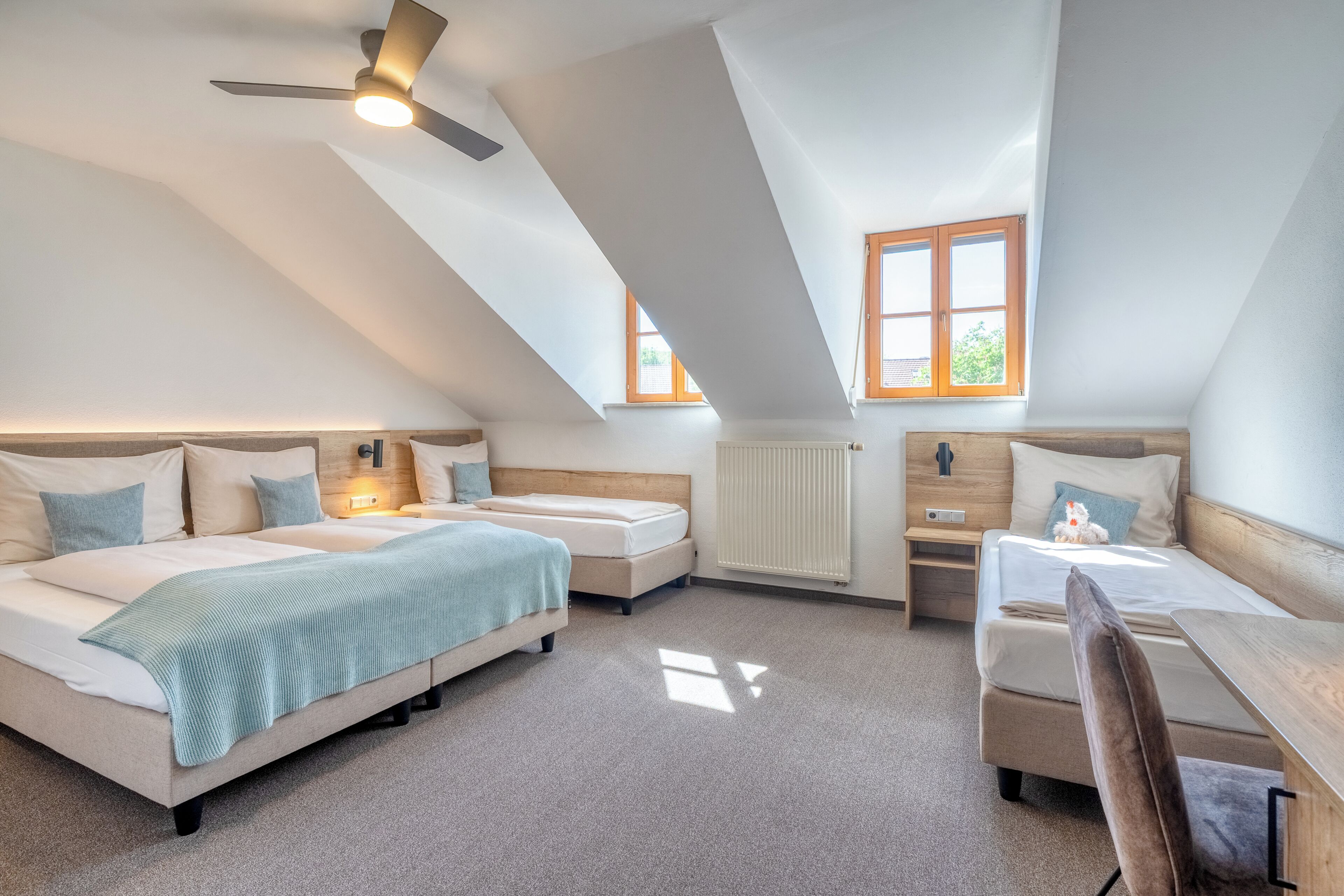A bedroom with a sloped ceiling, two beds, a desk, and a chair.