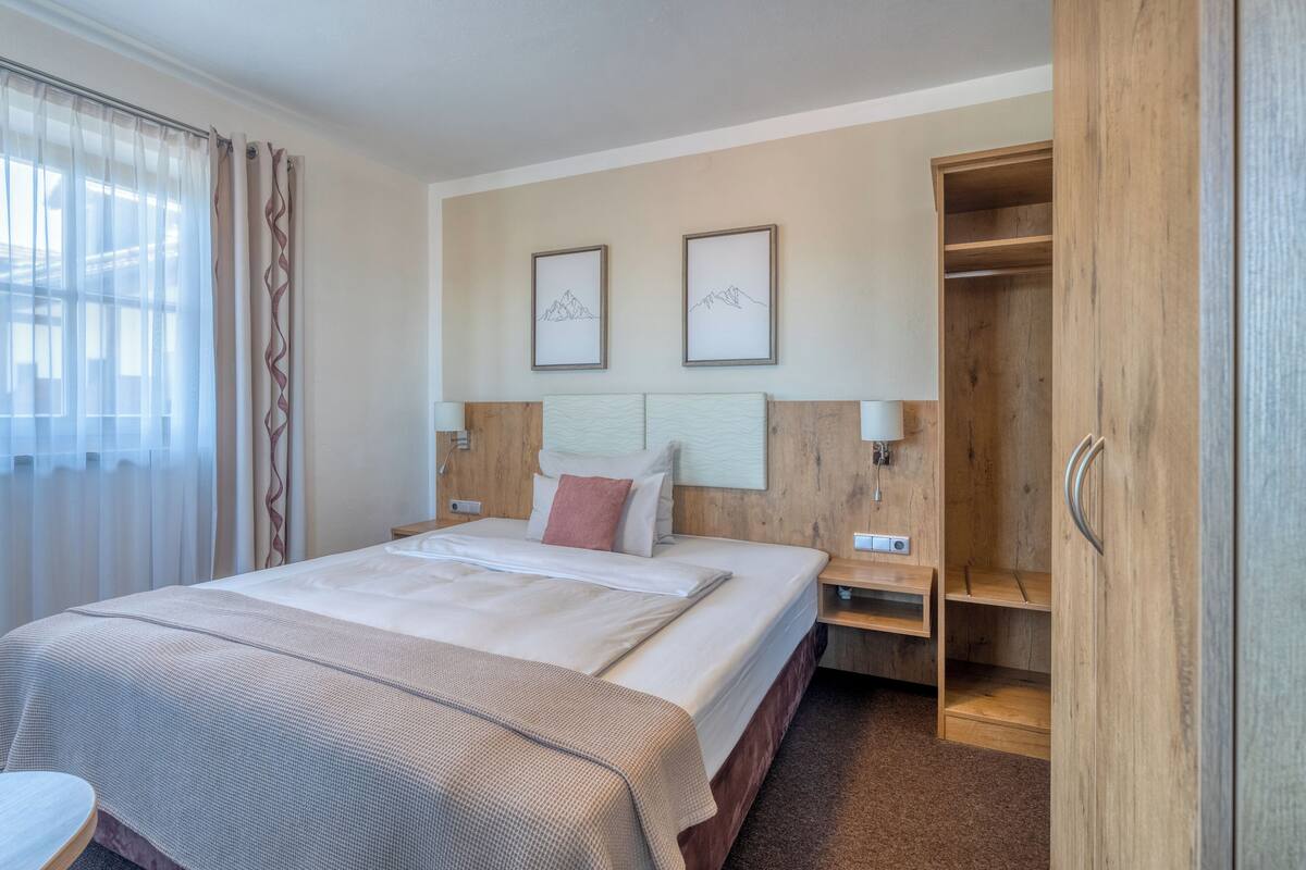 A hotel room with a bed, bedside tables, a wardrobe, and two framed pictures on the wall.