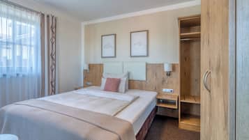 Una habitación de hotel con cama, mesitas de noche, un armario y dos cuadros en la pared.