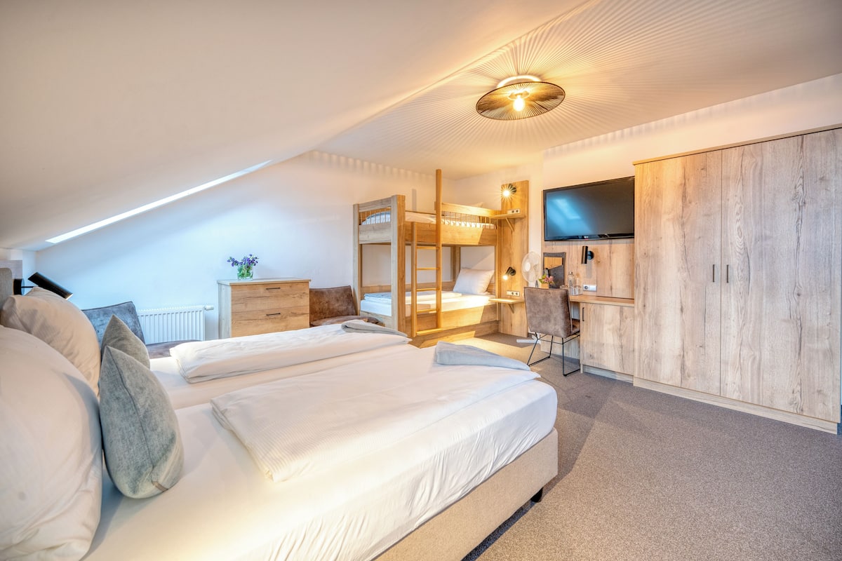 A bedroom with a bunk bed, a desk, a wardrobe, and a television.