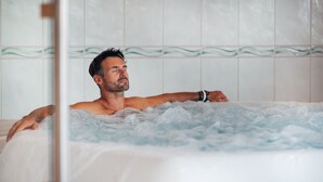 Een man ontspant in een jacuzzi, met een betegelde muur op de achtergrond.