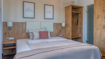 A hotel room with a large bed, wooden wardrobe, bedside tables, and wall-mounted artwork.