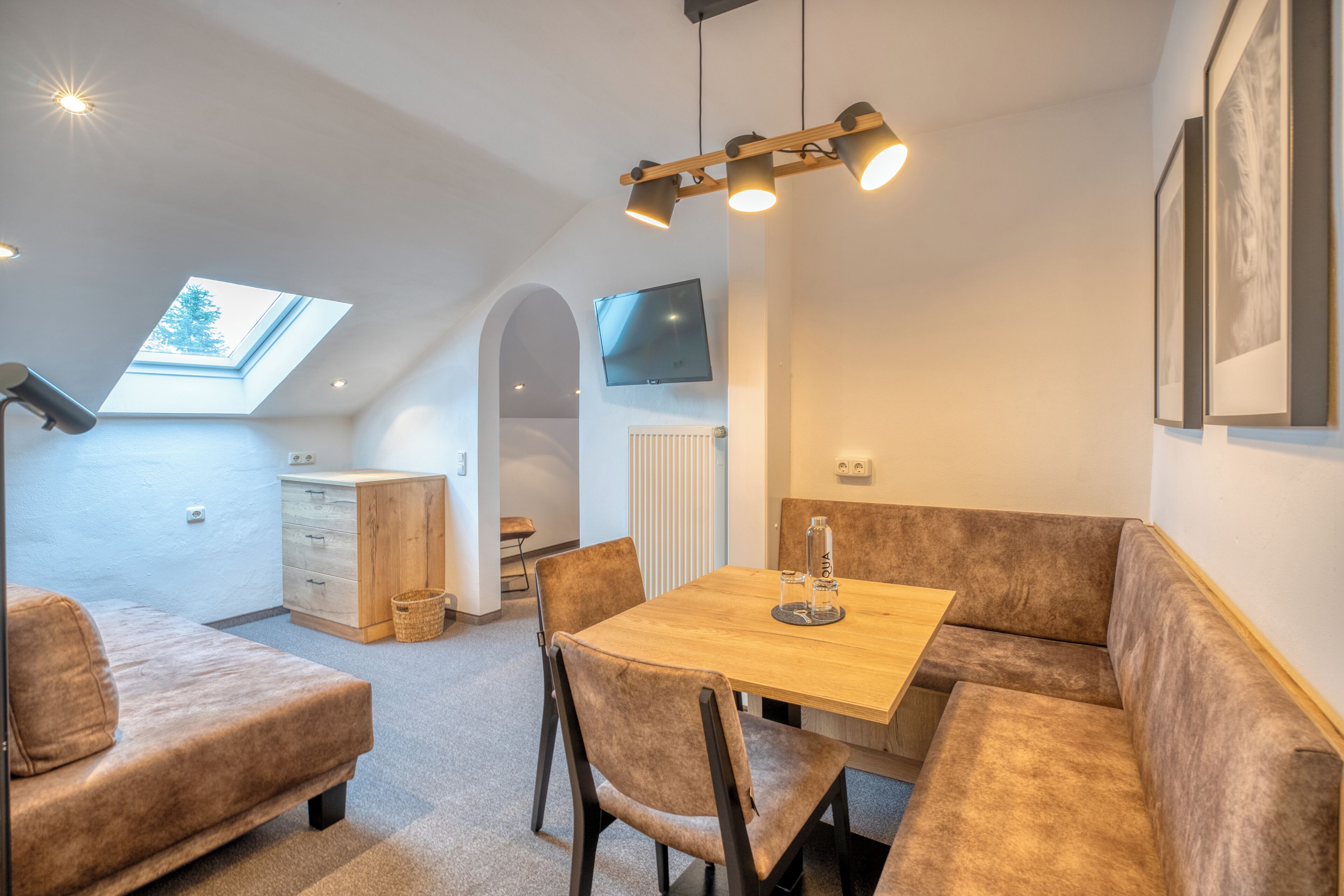Una habitación acogedora con cama en altillo, una mesa de comedor con sillas, un televisor montado en la pared y un tragaluz.