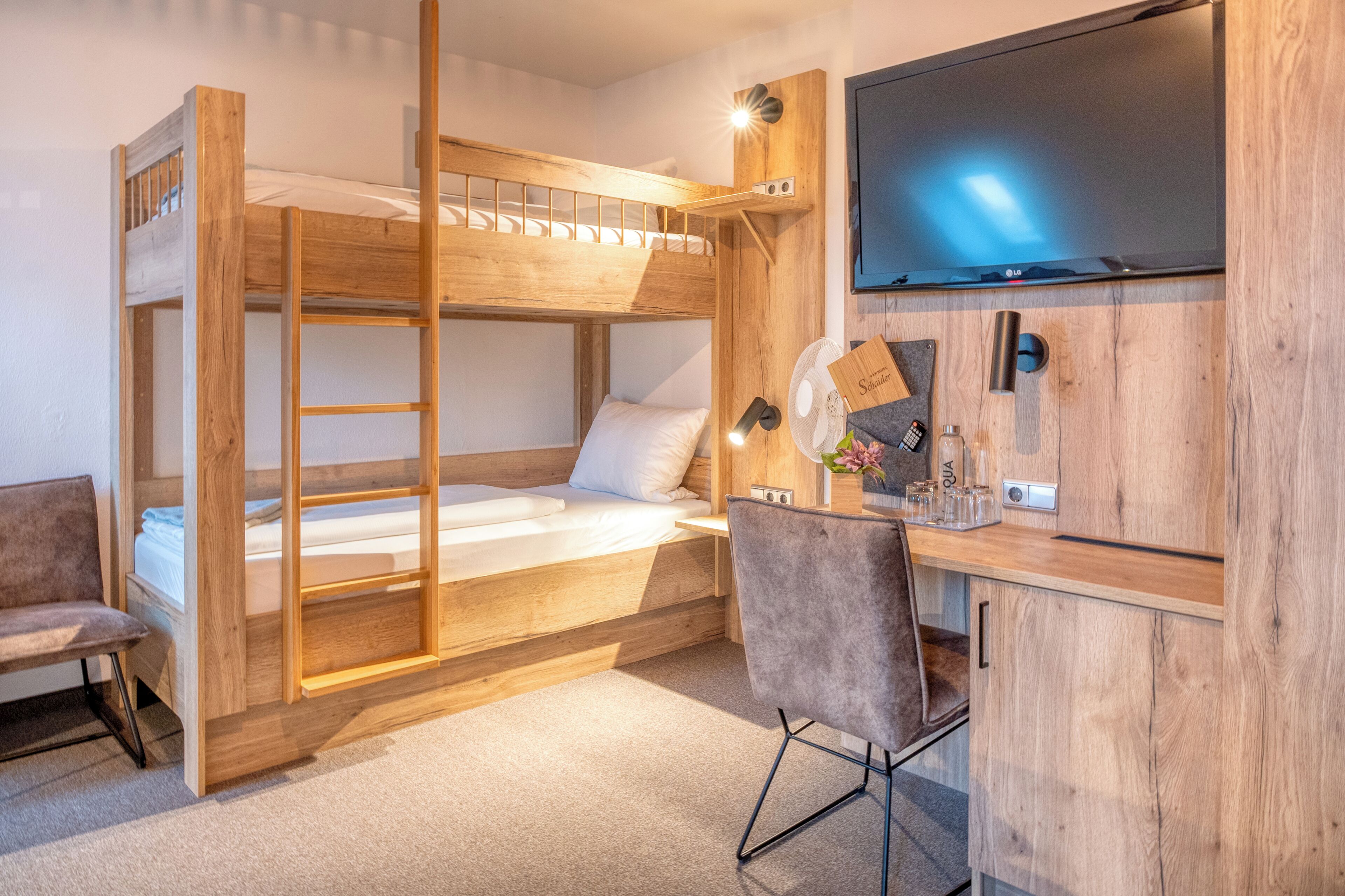 Ein Stockbett mit Schreibtisch und Stuhl, einem Flachbildfernseher und einem kleinen Schrank mit Ventilator und Dekoration.