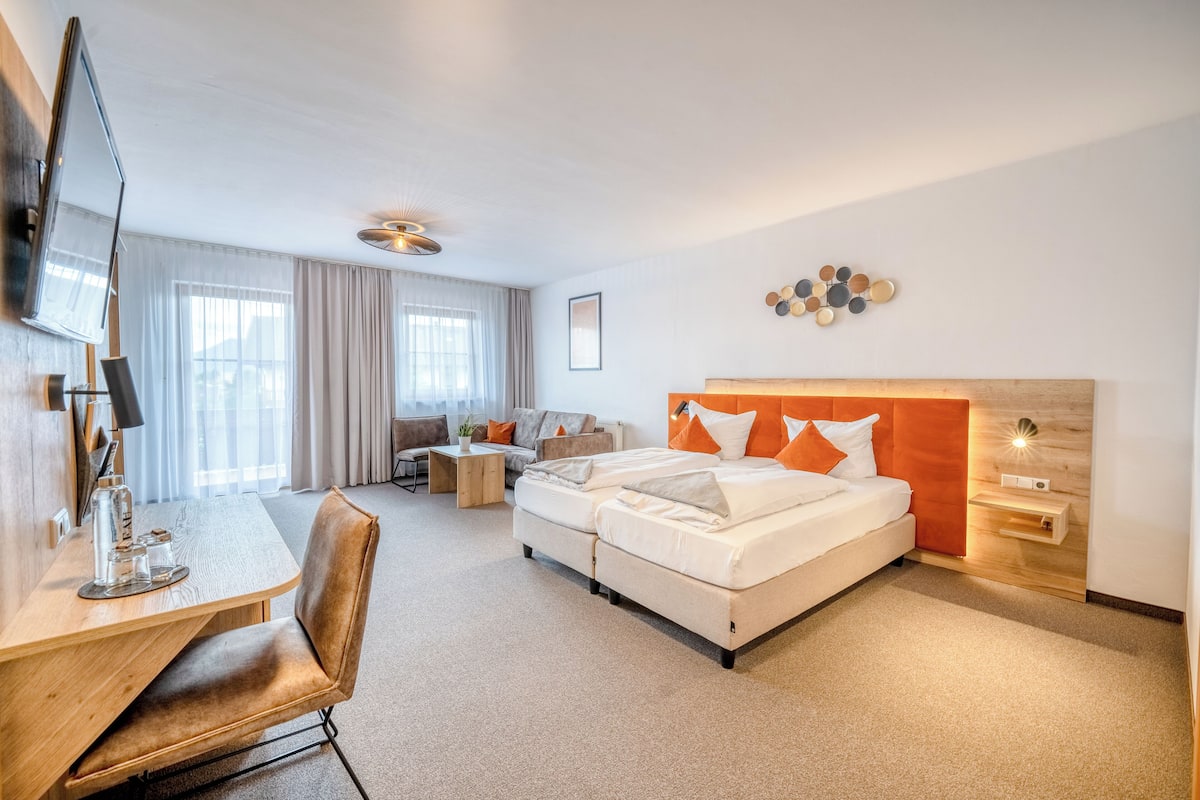 A hotel room with a bed, a desk, a chair, a TV, and a window with curtains.