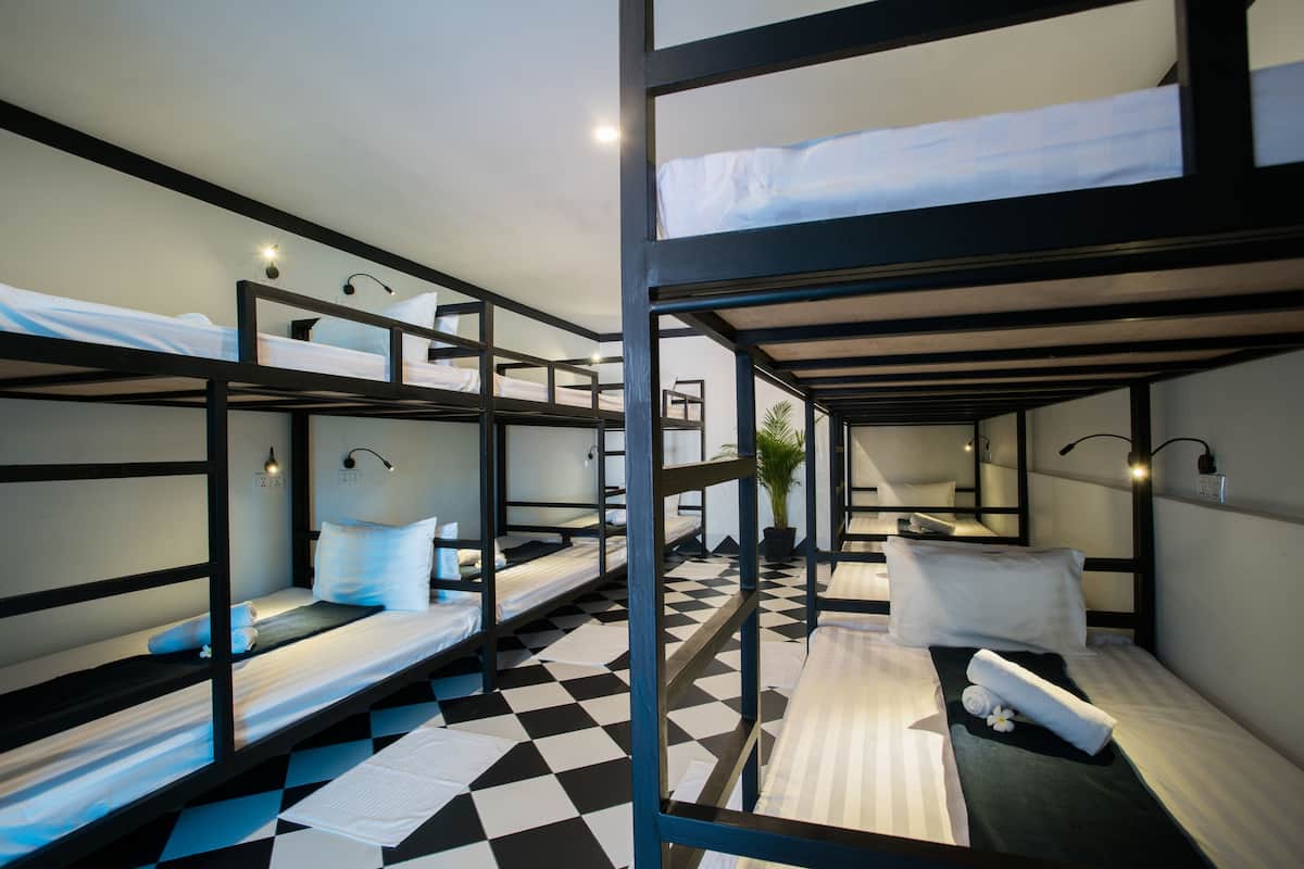 A dormitory-style room with bunk beds, a checkered floor, and wall-mounted lighting.