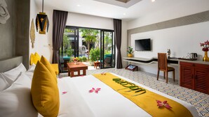 Habitación de hotel con una cama, un escritorio, una silla, un televisor y un ventanal corredero que da a un espacio exterior.