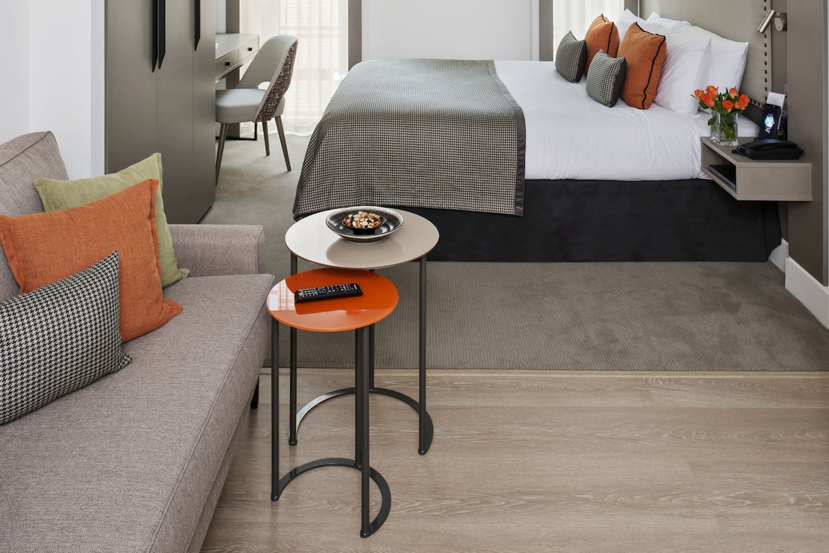 Una habitación de hotel moderna con una cama, un sofá, una mesita pequeña, un ventilador de techo y un escritorio.