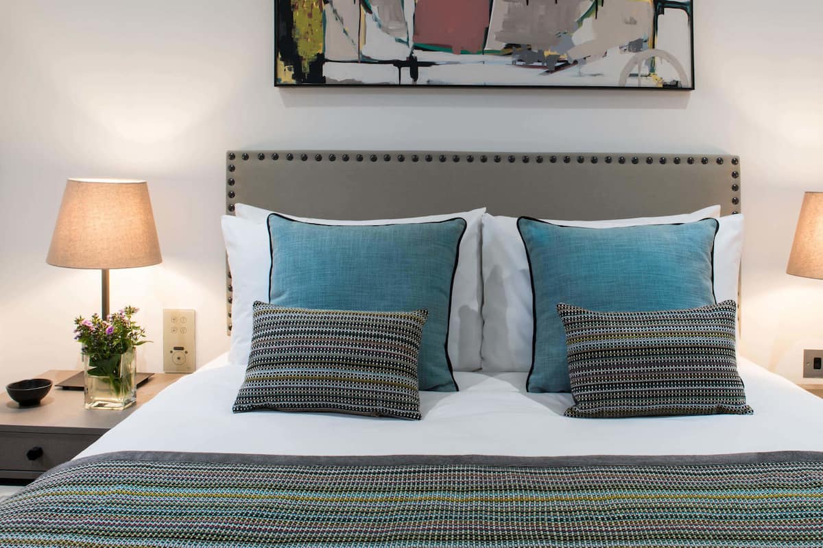 Una cama bien hecha con dos almohadas, una mesita de noche con una lámpara, un teléfono y un pequeño jarrón con flores.