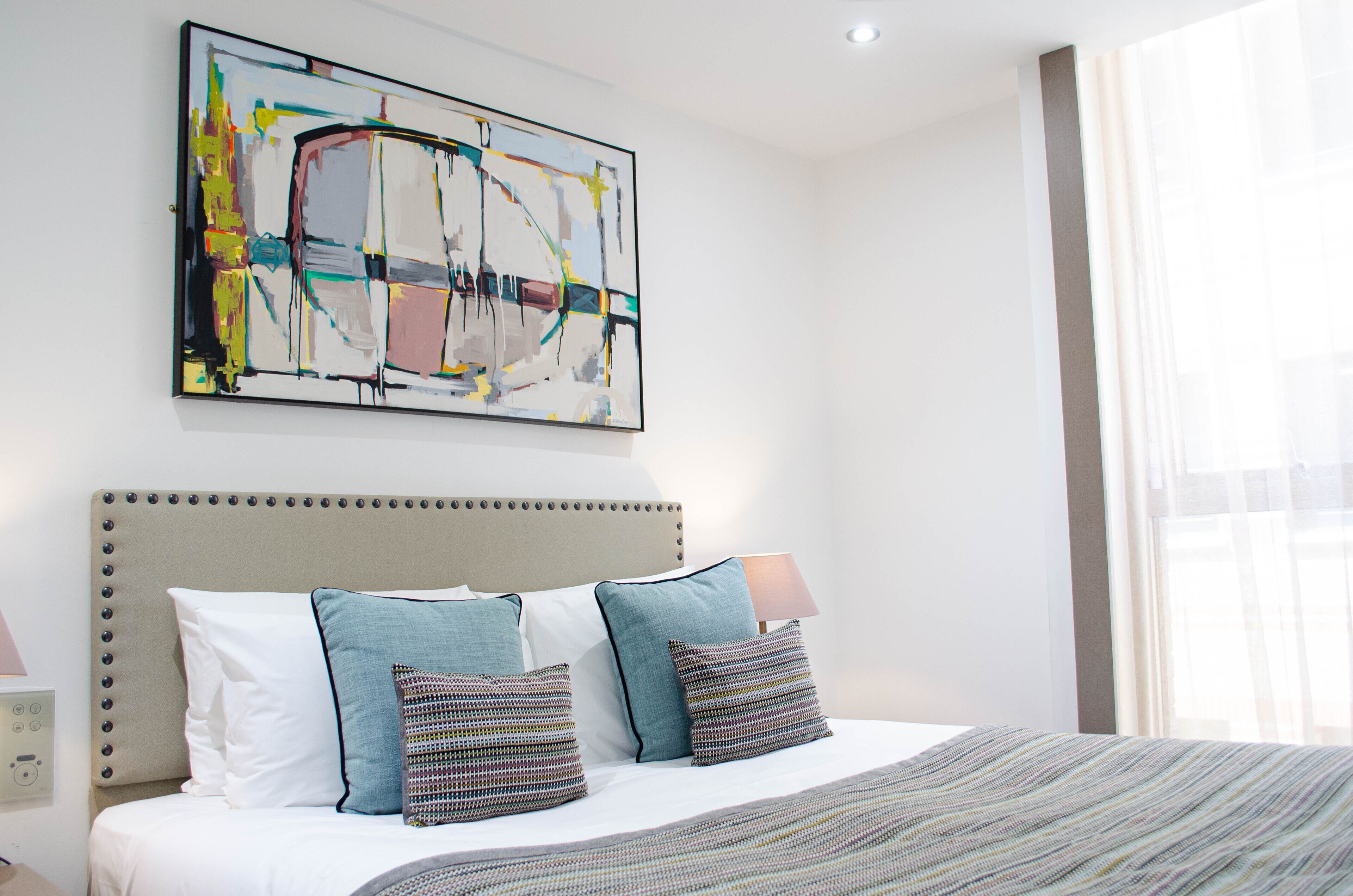 A hotel room with a large bed, a modern headboard, and a large abstract painting on the wall.