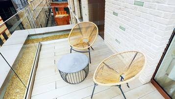 A balcony with two wicker chairs and a small round table, overlooking a city street.