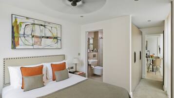 A hotel room with a large bed, a ceiling fan, a bathroom visible through an open door, and a dining area in the background.