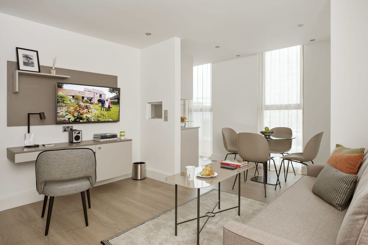 Una sala de estar moderna con televisor de pantalla plana, un sofá, una mesa de centro y un comedor con sillas.