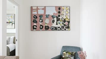 Een moderne woonkamer met een blauwe fauteuil, een klein rond tafeltje met een vaas, en een kleurrijk abstract schilderij aan de muur.